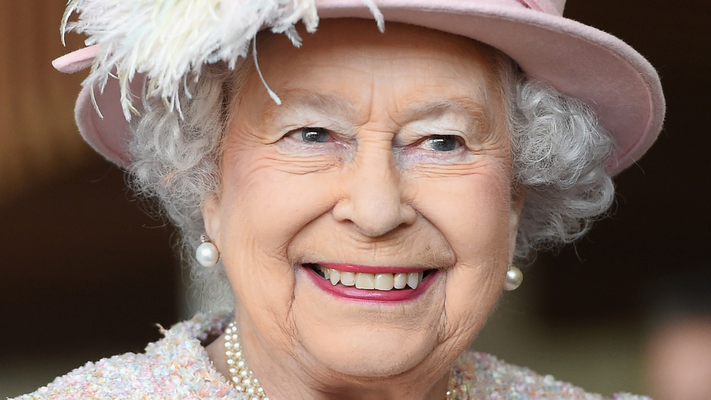 La reina Isabel II sonriendo en un evento vestida de rosa claro