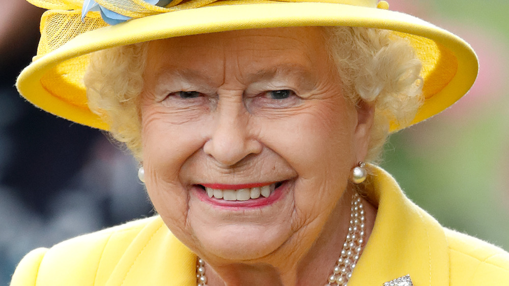 La reina Isabel II sonriendo con un traje amarillo y un sombrero a juego