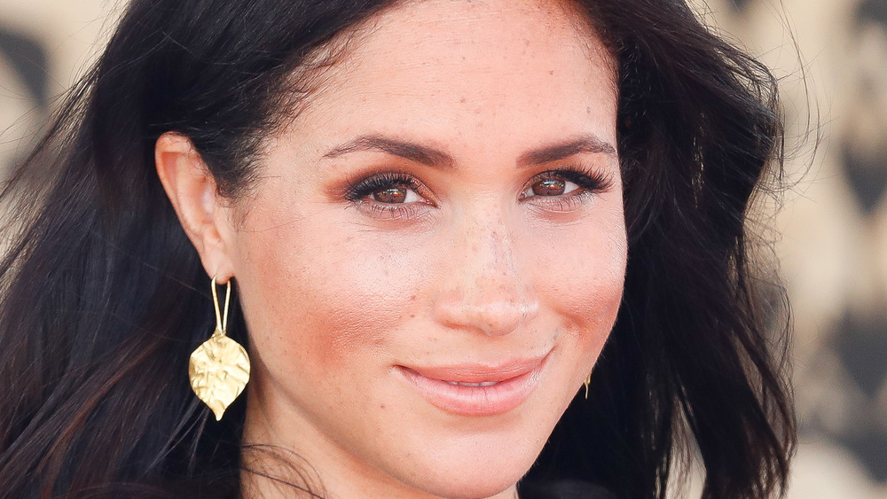 Meghan Markle sonriendo mientras usa aretes de pan de oro