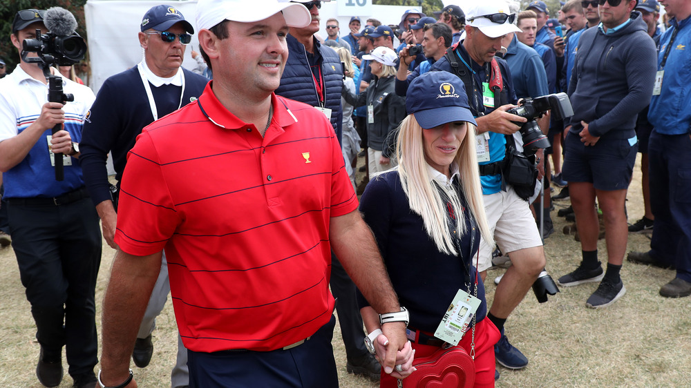 Patrick Reed y Justine Reed caminando de la mano, ambos con sombreros, rodeados de fotógrafos y fanáticos. 