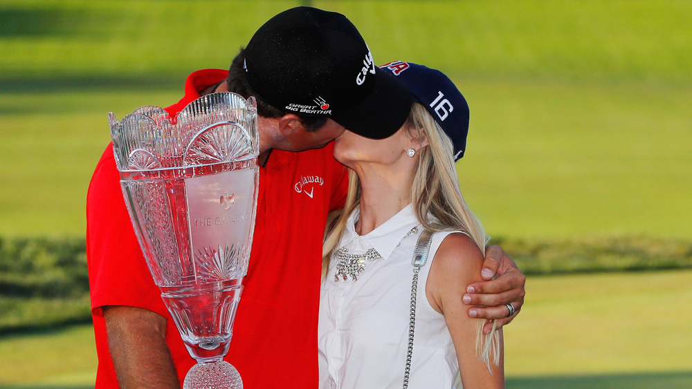 Patrick Reed y Justine Reed besándose, ambos con sombreros, en el campo de golf, con sombreros