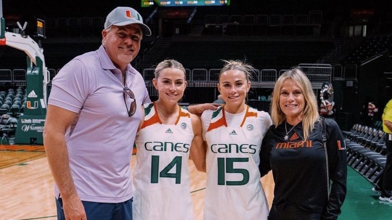 Los gemelos Cavinder con sus uniformes de Miami sonriendo junto a sus padres.