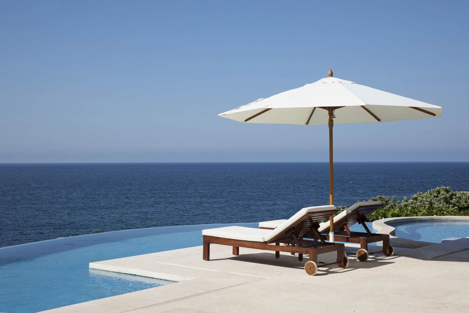 Reposeras bajo una sombrilla junto a una piscina infinita con vista al océano