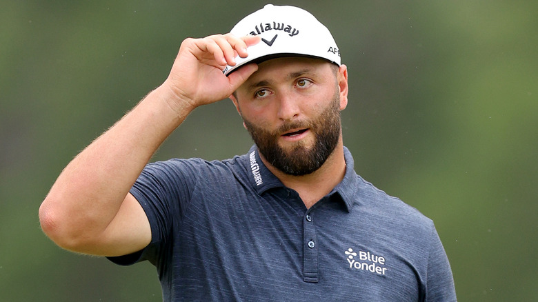 Jon Rahm arreglándose un sombrero en un campo de golf