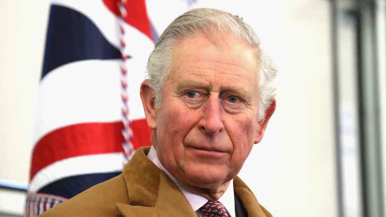 El rey Carlos III luce serio frente a la bandera británica